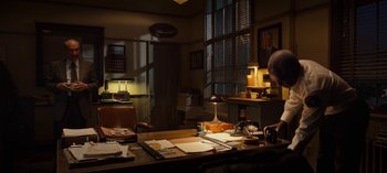 Movie still from “Guillermo del Toro's Cabinet of Curiosities” (2022), directed by Keith Thomas – A man sitting at a desk in front of a lamp; Wide shot, Low angle