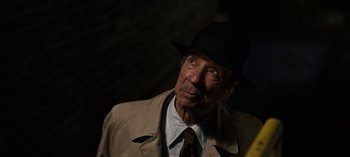 An older man wearing a hat and a trench coat