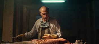 Movie still from “Guillermo del Toro's Cabinet of Curiosities” (2022), directed by Keith Thomas – An old man in an apron is looking at a piece of meat; Medium shot, Low angle