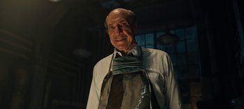 Movie still from “Guillermo del Toro's Cabinet of Curiosities” (2022), directed by Keith Thomas – An older man wearing an apron in a dimly - lit room; Close Up shot, Low angle