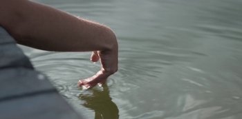 Movie still from “The Rain” (2018), created by Jannik Tai Mosholt – A hand reaching out of a body of water to catch a fish; Extreme Close Up shot, High angle