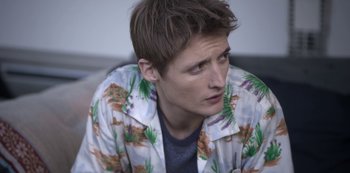 Movie still from “The Rain” (2018), created by Jannik Tai Mosholt – A young man wearing a floral shirt looks to his left; Close Up shot, Low angle