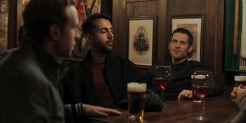 Movie still from “The Ritual” (2017), directed by David Bruckner – A group of men sitting at a table with drinks; Medium shot, Over the shoulder angle