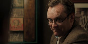 Movie still from “The Ritual” (2017), directed by David Bruckner – A person wearing glasses and a suit; Close Up shot, Over the shoulder angle