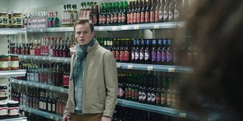 Movie still from “The Ritual” (2017), directed by David Bruckner – A man standing in front of shelves filled with bottles of alcohol; Medium shot, Over the shoulder angle