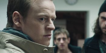 Movie still from “The Ritual” (2017), directed by David Bruckner – A man in a tan jacket looking at the camera with another man behind him; Close Up shot, Over the shoulder angle