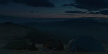 Movie still from “The Ritual” (2017), directed by David Bruckner – A group of people sitting on top of a grass covered field; Extreme Wide shot, High angle