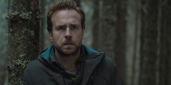 Movie still from “The Ritual” (2017), directed by David Bruckner – A person wearing a jacket near a forest; Close Up shot, Over the shoulder angle