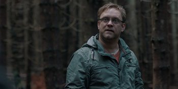 Movie still from “The Ritual” (2017), directed by David Bruckner – A man wearing a green jacket standing in front of trees; Close Up shot, Over the shoulder angle