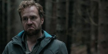 Movie still from “The Ritual” (2017), directed by David Bruckner – A person wearing a jacket near a forest; Close Up shot, Low angle