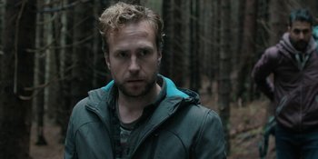 Movie still from “The Ritual” (2017), directed by David Bruckner – A person wearing a jacket in the woods; Close Up shot, Over the shoulder angle
