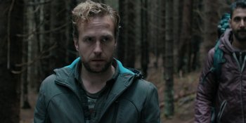 Movie still from “The Ritual” (2017), directed by David Bruckner – A person wearing a jacket near a forest; Close Up shot, Over the shoulder angle
