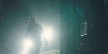 Movie still from “The Ritual” (2017), directed by David Bruckner – A man walking through a forest with a light shining on him; Wide shot, Low angle