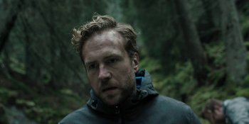 Movie still from “The Ritual” (2017), directed by David Bruckner – A person wearing a jacket near a forest; Close Up shot, Low angle