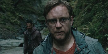Movie still from “The Ritual” (2017), directed by David Bruckner – A man with glasses is standing next to another man in the woods; Close Up shot, Over the shoulder angle