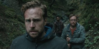 Three men are walking through the woods in the rain