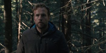 Movie still from “The Ritual” (2017), directed by David Bruckner – A person wearing a jacket near a forest; Close Up shot, Low angle