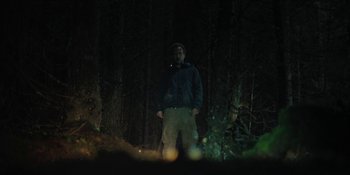 Movie still from “The Ritual” (2017), directed by David Bruckner – A man standing in the dark in the woods; Wide shot, Low angle