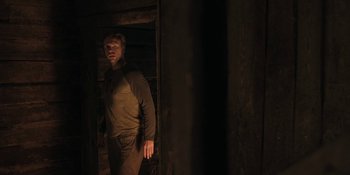 Movie still from “The Ritual” (2017), directed by David Bruckner – A man standing next to a door in a dark room; Medium shot, Over the shoulder angle