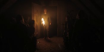Movie still from “The Ritual” (2017), directed by David Bruckner – A man standing in a room holding a fire; Wide shot, Over the shoulder angle