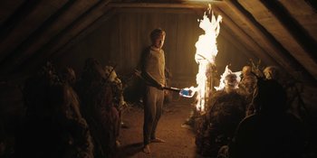 Movie still from “The Ritual” (2017), directed by David Bruckner – A person holding a fire in a room; Wide shot, Low angle
