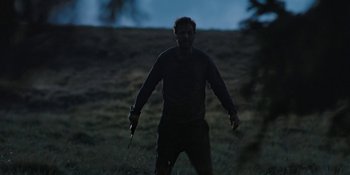 Movie still from “The Ritual” (2017), directed by David Bruckner – A man standing in the middle of a field holding a knife; Medium shot, Low angle