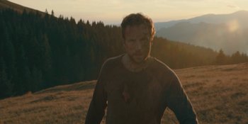 Movie still from “The Ritual” (2017), directed by David Bruckner – A man in a brown shirt standing in a field; Medium shot, Low angle
