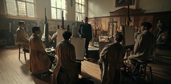 Movie still from “Guillermo del Toro's Cabinet of Curiosities” (2022), directed by Keith Thomas – A group of people sitting in a room with paintings on easels; Wide shot, Low angle