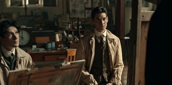 Movie still from “Guillermo del Toro's Cabinet of Curiosities” (2022), directed by Keith Thomas – A man wearing a suit and tie standing in front of a painting; Medium shot, Over the shoulder angle