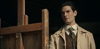 Movie still from “Guillermo del Toro's Cabinet of Curiosities” (2022), directed by Keith Thomas – A man wearing a suit and tie standing in front of an easel; Close Up shot, Low angle