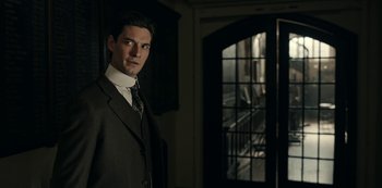 Movie still from “Guillermo del Toro's Cabinet of Curiosities” (2022), directed by Keith Thomas – A man in a suit and tie standing in front of an open door; Medium shot, Low angle