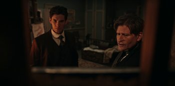 Movie still from “Guillermo del Toro's Cabinet of Curiosities” (2022), directed by Keith Thomas – Two men in suits standing in a living room; Medium shot, Over the shoulder angle
