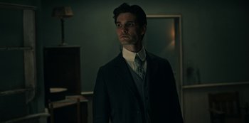 Movie still from “Guillermo del Toro's Cabinet of Curiosities” (2022), directed by Keith Thomas – A man in a suit and tie standing in a room; Close Up shot, Low angle