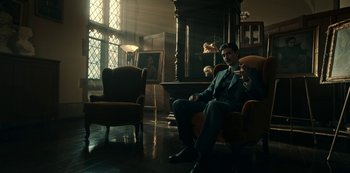Movie still from “Guillermo del Toro's Cabinet of Curiosities” (2022), directed by Keith Thomas – A man in a suit sitting in a chair in a living room; Wide shot, Low angle