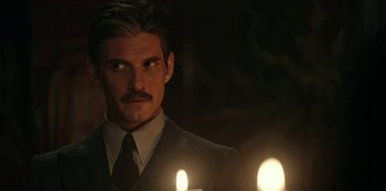 Movie still from “Guillermo del Toro's Cabinet of Curiosities” (2022), directed by Keith Thomas – A man in a suit and tie with two lit candles in front of him; Close Up shot, Over the shoulder angle