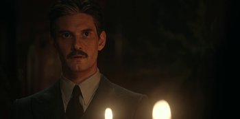 Movie still from “Guillermo del Toro's Cabinet of Curiosities” (2022), directed by Keith Thomas – A man in a suit and tie standing in front of two candles; Close Up shot, Low angle