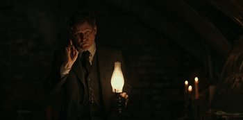 Movie still from “Guillermo del Toro's Cabinet of Curiosities” (2022), directed by Keith Thomas – A man in a suit and tie holding an oil lamp in the dark; Medium shot, Low angle