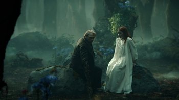A man kneeling down next to a woman in a white dress