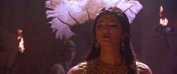 Movie still from “The Scorpion King” (2002), directed by Chuck Russell – A woman in a gold costume with feathers on her head; Close Up shot, Low angle