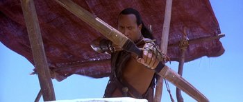Movie still from “The Scorpion King” (2002), directed by Chuck Russell – A man holding a long wooden stick in his hands; Medium shot, Over the shoulder angle