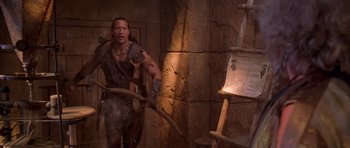 Movie still from “The Scorpion King” (2002), directed by Chuck Russell – A man holding an axe in front of an easel; Medium shot, Over the shoulder angle