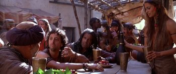 Movie still from “The Scorpion King” (2002), directed by Chuck Russell – A group of people sitting at a table eating food; Medium shot, Over the shoulder angle