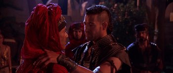 Movie still from “The Scorpion King” (2002), directed by Chuck Russell – A man with a shaved head and a red head covering is talking to another man; Close Up shot, Over the shoulder angle