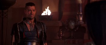 Movie still from “The Scorpion King” (2002), directed by Chuck Russell – A man in a leather vest standing in front of a fireplace; Medium shot, Over the shoulder angle