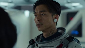Movie still from “The Silent Sea” (2021), created by Choi Hang-Yong – A man in a spacesuit with ear buds in his ears; Close Up shot, Over the shoulder angle