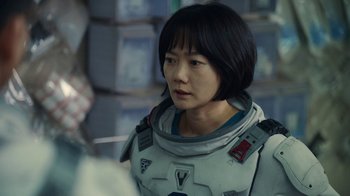 Movie still from “The Silent Sea” (2021), created by Choi Hang-Yong – A woman in a spacesuit is standing in a room; Close Up shot, Over the shoulder angle