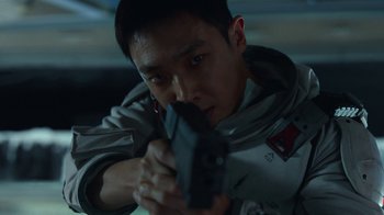 Movie still from “The Silent Sea” (2021), created by Choi Hang-Yong – A man holding a gun while wearing a jacket; Close Up shot, Low angle