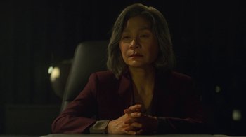 Movie still from “The Silent Sea” (2021), created by Choi Hang-Yong – An older woman sitting at a table in a dark room; Close Up shot, Over the shoulder angle