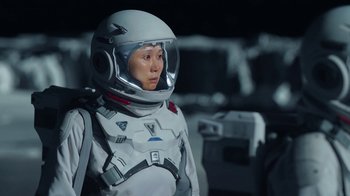 Movie still from “The Silent Sea” (2021), created by Choi Hang-Yong – A woman in a spacesuit and helmet standing in the dark; Medium shot, Over the shoulder angle