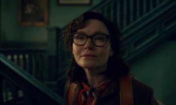 Movie still from “Guillermo del Toro's Cabinet of Curiosities” (2022), directed by Keith Thomas – A woman wearing glasses standing in front of a staircase; Close Up shot, Low angle